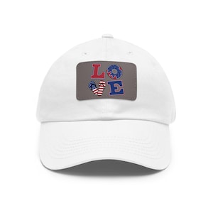 May include: A white baseball cap featuring a rectangular patch on the front. The patch is grey and displays the word LOVE in large letters. The letter O is replaced by a blue donut, and the letter V is replaced by a pair of American flag flip-flops.