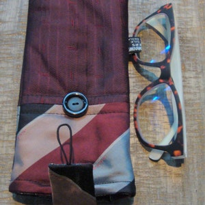 May include: A handmade glasses case and a pair of eyeglasses. The case is made of burgundy and striped fabric with a black button closure. The eyeglasses have a tortoiseshell pattern frame. A small, square, leather-like tag hangs from the case.