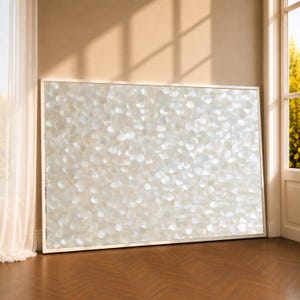 May include: A large rectangular wall art piece featuring a dense, textured surface of overlapping white, iridescent, petal-like shapes. The artwork is encased in a thin, light-colored frame, creating a shimmering, reflective effect across the entire surface.
