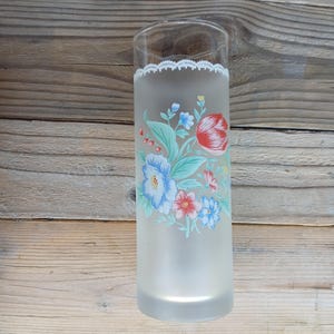 Peut inclure: Un verre cylindrique en verre dépoli orné d'une bordure blanche ressemblant à de la dentelle près du rebord et d'un bouquet de fleurs coloré dans des tons de rouge, bleu et vert centré sur la surface avant du verre.
