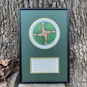 May include: A framed print of a Brigid's Cross, a traditional Irish symbol made of woven straw, with a green background and a gold border. The print includes a poem about Brigid, the Celtic goddess of healing, poetry, and smithcraft.