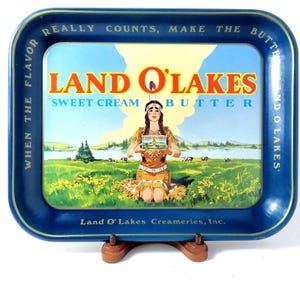 May include: A rectangular blue metal serving tray featuring a vintage Land O'Lakes Sweet Cream Butter advertisement. The center depicts a person in traditional attire holding a butter box, with a landscape of cows, grass, and water.
