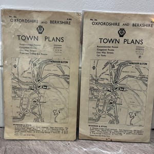 Op de afbeelding: Twee vintage papieren kaarten getiteld Oxfordshire and Berkshire Town Plans, elk in een doorzichtige plastic hoes. De kaarten bevatten zwarte inkt op gebroken wit papier en tonen de stratenplannen van Windsor en Eton met legenda's.