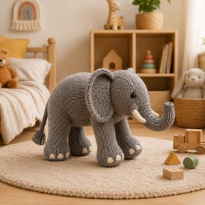 May include: A gray knitted elephant toy featuring a textured surface, large ears, a curved trunk, two white tusks, and small white accents on the feet. The elephant has black button eyes and a tail with a small tassel at the end.