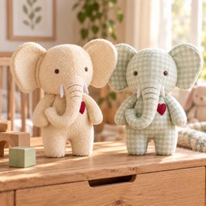 May include: Two plush elephant toys standing side by side. The left elephant is solid cream with white polka-dot ears, while the right elephant features a light green and white gingham pattern. Both have dark eyes, white tusks, and a red heart.