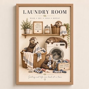 May include: A framed wall art print titled LAUNDRY ROOM featuring otters doing laundry. Text includes WASH DRY FOLD REPEAT, HELP WANTED APPLY TO THE OTTERS, and LOST SOCKS SEEKING SOLE MATES. The otters are shown with baskets, a washing machine, and socks.