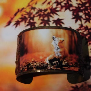 May include: A copper cuff bracelet with a printed image of a red fox howling at the sunset in a forest setting.