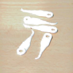 May include: A collection of four small, white, elongated charms with a smooth, matte finish. Each charm features a distinct, slightly curved shape and a small circular hole at one end, designed for attachment to jewelry or other decorative items.
