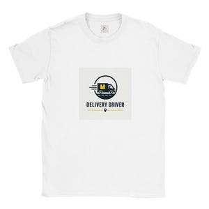 May include: A white short-sleeved t-shirt featuring a central graphic of a dark blue delivery truck inside a circle with a yellow package. Below the truck, the text reads DELIVERY DRIVER in bold dark blue letters with a horizontal line and a location pin.
