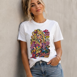 May include: A white short-sleeved t-shirt featuring a colourful graphic print of a blonde woman with a guitar, butterflies, and cowboy boots. The design includes text reading Jolene, 9 to 5, I Will Always Love You, and Dollywood, Tennessee.
