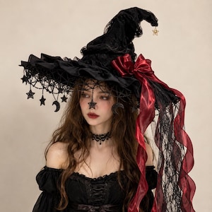 May include: A black pointed hat featuring a wide, ruffled brim adorned with hanging black star and crescent moon charms. The hat is decorated with a deep red satin ribbon bow and long, flowing red and black lace ribbons trailing down the side.