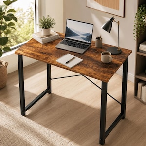 May include: A rectangular desk with a rustic brown wood-grain surface and a black metal frame. The desk features X-shaped support bars on the sides and back. It is topped with a laptop, a small potted plant on books, a notebook, and a desk lamp.