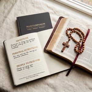 May include: A black Mass Companion book, an open journal with sections for Gratitude, Personal Intentions, and People to Pray For, and an open Bible with a wooden rosary featuring a crucifix resting on the pages, all arranged together.