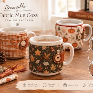 May include: A reversible fabric mug cozy sewing pattern featuring three white ceramic mugs wrapped in fabric sleeves with autumn-themed prints including orange pumpkins, brown leaves, and orange plaid patterns, each secured with a single wooden button.