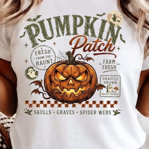 May include: A white t-shirt featuring a graphic print with the text PUMPKIN PATCH, FRESH FROM THE HAUNT, FARM FRESH, GHASTLY GROWN, and SKULLS GRAVES SPIDER WEBS. The design includes a central orange jack-o'-lantern, a ghost, and a witch silhouette.