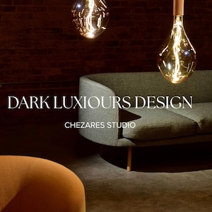 Op de afbeelding: Drie amberkleurige glazen hanglampen met zichtbare filamenten hangen boven een gebogen grijze bank en een deel van een oranje stoel. De tekst "DARK LUXIOURS DESIGN" en "CHEZARES STUDIO" is in het wit over de afbeelding geplaatst.