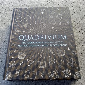 May include: A hardcover book titled "QUADRIVIUM" with the subtitle "THE FOUR CLASSICAL LIBERAL ARTS OF NUMBER, GEOMETRY, MUSIC, & COSMOLOGY." The cover is dark brown with white geometric shapes and symbols.
