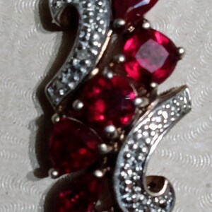 May include: A silver pendant with a cluster of red gemstones set in a swirl design.