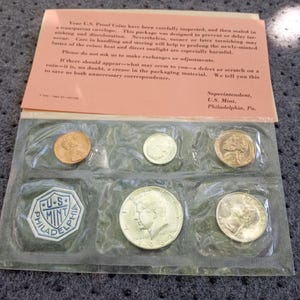 Könnte beinhalten: Ein U.S. Mint Proof Münzensatz, versiegelt in einem transparenten Umschlag. Das Set enthält verschiedene Münzen, darunter ein Penny, ein Dime und ein Half Dollar. Die Verpackung enthält Text zur Münzpflege und -aufbewahrung.
