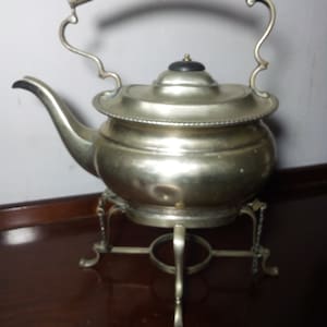 May include: A silver teapot with a black wooden handle and a stand. The teapot has a round body and a lid with a knob. The stand has three legs and a ring in the center.
