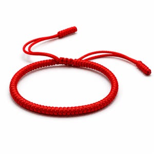 Può includere: Un braccialetto in corda rosso brillante con una trama intrecciata. Il braccialetto include un meccanismo a nodo scorsoio regolabile con due estremità libere, ciascuna rifinita con un piccolo nodo rosso cilindrico e ben stretto.