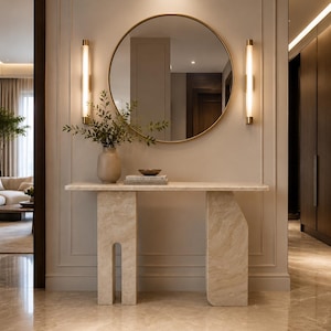 May include: A beige stone console table with a rectangular top and two asymmetrical legs, featuring a round gold-framed mirror above it. Two vertical wall sconces flank the mirror, while a ceramic vase with greenery sits on the table.