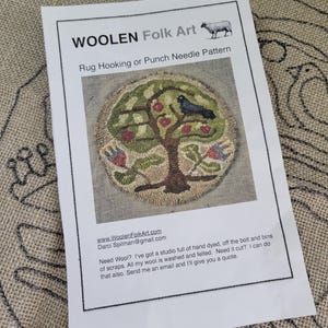 May include: A printed paper sheet titled WOOLEN Folk Art Rug Hooking or Punch Needle Pattern. It features a circular image of a tree with green leaves, red apples, and a black bird, plus contact information for WoolenFolkArt.com and Darci Spilman.