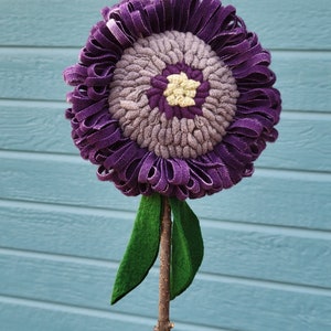 May include: A purple felt flower with a textured center and green felt leaves attached to a brown stick.