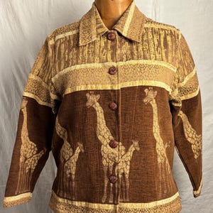 May include: A long-sleeved button-down jacket in shades of brown and tan. The garment features a woven giraffe pattern across the lower section and a textured, abstract design on the upper chest, shoulders, and collar, finished with dark buttons.