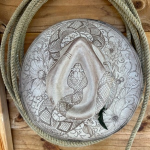 May include: A white cowboy hat with a detailed design of a snake and flowers. The snake has a silver nose ring and silver eyes.
