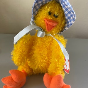 May include: Yellow plush chick toy wearing a blue and white gingham bonnet with a white ribbon tied around its neck. The chick has orange feet and a red beak. The toy has a Ty Beanie Baby tag attached.