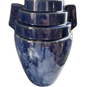 May include: A blue and white ceramic vase with a unique layered design and two handles. The vase has a mottled blue glaze with white streaks.