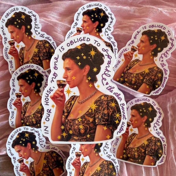 May include: A collection of die-cut stickers featuring a woman in a dark patterned dress holding a glass, surrounded by gold star accents. The text reads: IN OUR HOUSE, NO ONE IS OBLIGED TO SPARKLE, the other Bennet sister. The stickers are identical.