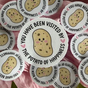 May include: A collection of circular white stickers featuring a cartoon potato with a smiling face and pink cheeks. The text around the potato reads, "YOU HAVE BEEN VISITED BY THE POTATO OF HAPPINESS," accented with small pink hearts.