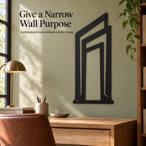 May include: A black metal wall art piece featuring geometric architectural lines. The text on the wall reads: Give a Narrow Wall Purpose. Architectural lines without a bulky frame. The design consists of vertical and angled bars in a frame-like structure.