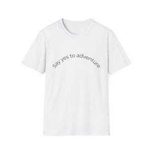 Puede incluir: Una camiseta blanca de manga corta con el texto negro "Say yes to adventure" impreso en un ligero arco sobre el pecho. La prenda tiene un cuello redondo y un corte estándar, ofreciendo un aspecto limpio y sencillo para el uso diario.