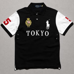 May include: A black polo shirt with white sleeves, featuring the text TOKYO in white across the chest. It includes a white embroidered Polo Ralph Lauren horse logo, a gold crest with a Japanese flag, and a red number 5 on the right sleeve.