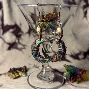 May include: A pair of iridescent abalone shell earrings with pink wire wrapping and white bead accents. The earrings are shaped like crescent moons.