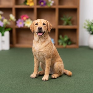 May include: A needle-felted sculpture of a golden-coloured Labrador retriever dog sitting in an upright position. The dog has a textured coat, floppy ears, a dark nose, and an open mouth with a visible pink tongue, capturing a realistic appearance.