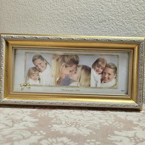May include: A rectangular gold and white picture frame with an ornate embossed border. The frame contains three photographs of a woman and a child, with a small gold bow accent in the corner and the text "We love you! 2006" printed at the bottom.