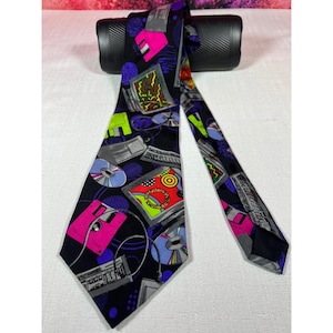 May include: A black necktie featuring a vibrant 1990s-style computer technology print. The pattern includes bright pink floppy disks, colourful compact discs, keyboards, and computer monitors scattered across the fabric in shades of neon green, blue, and red.