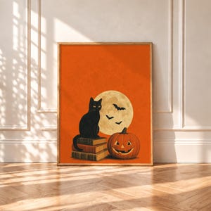 Può includere: Una stampa artistica da parete incorniciata raffigurante un gatto nero seduto su una pila di tre libri antichi accanto a una zucca intagliata arancione. Una grande luna piena giallo pallido con tre piccoli pipistrelli neri che volano davanti si staglia su uno sfondo arancione.