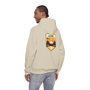 May include: A beige hooded sweatshirt featuring a graphic on the back with the text Less Wifi, More Wild Life. The design depicts a sunset over a forest with two small tents and a lake, enclosed within a shield-shaped border in black and yellow.