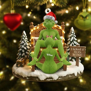 Peut inclure: Une décoration de Noël représentant deux personnages verts dans un lit. L'un porte un bonnet de Père Noël avec le nom Robert, l'autre a le nom Tiffany dans le dos. Un panneau en bois indique I licked it So it's MINE.