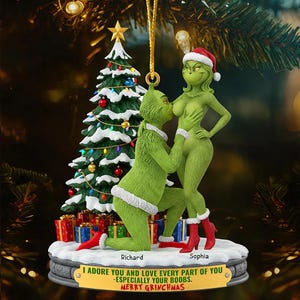 Puede incluir: Un adorno navideño con dos figuras verdes tipo Grinch, una arrodillada y otra de pie, junto a un árbol decorado. La base muestra los nombres Richard y Sophia, con el texto: I ADORE YOU AND LOVE EVERY PART OF YOU -ESPECIALLY YOUR BOOBS. MERRY GRINCHMAS.