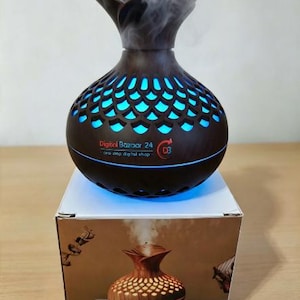 May include: A dark brown, vase-shaped essential oil diffuser with a cutout scale pattern emitting a blue light and mist. The device features the text Digital Bazaar 24 and a logo. It sits atop its product box, which displays a 300ml capacity label.