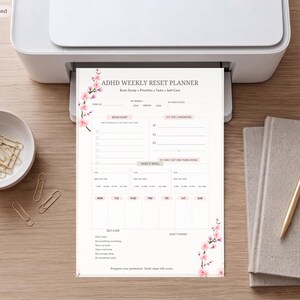 May include: A white paper ADHD weekly reset planner featuring pink cherry blossom illustrations on the top left and bottom right corners. The layout includes sections for brain dump, priorities, tasks, self-care, and a daily schedule for the week.