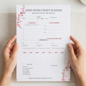 May include: A white ADHD Weekly Reset Planner sheet featuring pink cherry blossom illustrations on the top left and bottom right corners. The layout includes sections for Brain Dump, Top 3 Priorities, tasks, daily scheduling, and self-care checklists.