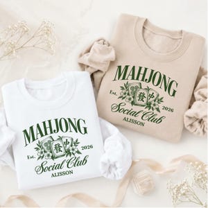 May include: A white and a beige crewneck sweatshirt, each featuring a dark green graphic with the text "MAHJONG SOCIAL CLUB", "Est. 2026", and "ALISSON", accompanied by illustrations of mahjong tiles and small floral accents.