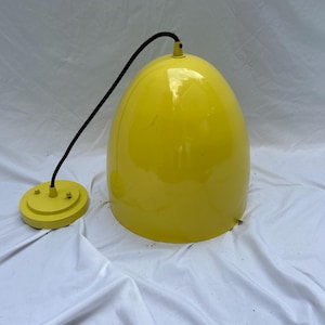 May include: A bright yellow pendant lamp with a smooth, glossy, dome-shaped shade. The lamp features a black electrical cord connected to a matching yellow circular ceiling canopy. The design is simple and functional with a solid color finish.